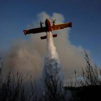 A firefighting airplane makes a water drop as a wildfire burns near the village of Metochi, north of Athens, Monday. | REUTERS