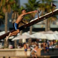A competitor tries to grab a flag as he falls off the gostra, a wooden pole covered in lard, during the main competition, part of the celebrations on the religious feast day of St Julian, patron of the town of St. Julian’s, Malta, Sunday. Malta festival-goers climb the larded log for flags, glory, splashdown