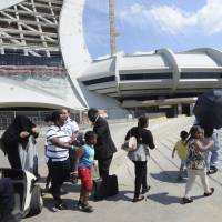 Asylum seekers take a walk outside Olympic Stadium as security guards look on in Montreal Wednesday. The stadium will be housing asylum seekers after a spike in the number of people crossing at the United States border in recent months. | RYAN REMIORZ / THE CANADIAN PRESS / VIA AP