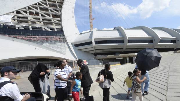 Asylum seekers take a walk outside Olympic Stadium as security guards look on in Montreal Wednesday. The stadium will be housing asylum seekers after a spike in the number of people crossing at the United States border in recent months. Montreal's Olympic Stadium opens for asylum seekers coming from U.S.
