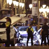 Police officers stand next to the van involved on an attack in Las Ramblas in Barcelona, Spain, Thursday. The white van jumped up onto a sidewalk and sped down a pedestrian zone Thursday in Barcelona’s historic Las Ramblas district, swerving from side to side as it plowed into tourists and residents. Police said 13 people were killed and more than 50 wounded in what they called a terror attack. One held after attacker drives van into crowd on Barcelona promenade, killing 13, wounding over 50
