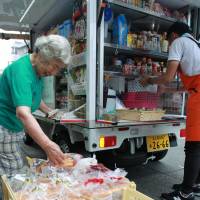 An elderly woman checks items in a mobile supermarket in front of her home in Minato Ward, Nagoya. Aichi's mobile supermarkets keeps seniors stocked with groceries, checks in on aging customers