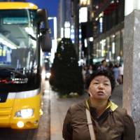A Chinese tourist waits for a tour bus in Tokyo’s Ginza district in April 2016. Tourist spending up in Japan as foreign travelers take in more cultural experiences