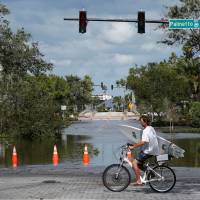 A man carrying a surf board bikes past a flooded street after Hurricane Irma made landfall in Daytona Beach, Florida, Monday. EPA gives Florida utilities two-week blanket pass to pollute after Irma leaves 6.5 million without power