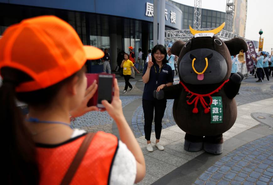A visitor poses for a photographer with official cattle mascot Ushi-Masamune at the 11th National Japanese Beef Ability Expo in Sendai.