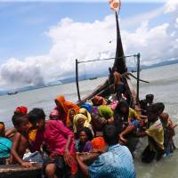 Smoke is seen on Myanmar’s side of border as Rohingya refugees get off a boat after crossing the Bangladesh-Myanmar border through the Bay of Bengal in Shah Porir Dwip, Bangladesh, Monday. Bangladesh offers land to shelter thousands of Rohingya fleeing Myanmar as camps burst at seams