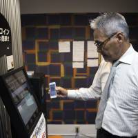 An employee using a smartphone demonstrates a bitcoin ATM at the Coin Trader bitcoin retail store at the Nakano Broadway complex in Tokyo’s Nakano Ward on Wednesday. Cryptocurrencies threaten central banks' control over money supply — and officials study using their technology
