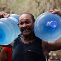 A man carries two jugs filled with water collected from a natural spring created by the landslides in a mountain next to a road in Corozal, west of San Juan Sunday following the passage of Hurricane Maria. Aid finally reaching hurricane-hammered Puerto Rico as hysteria spreads
