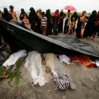 People cover the bodies of Rohingya refugee women and children who died after their boat capsized while crossing the border through the Bay of Bengal, at Shah Porir Dwip, near Teknaf, Bangladesh, Thursday. At least 18 Rohingya women, kids die in desperate boat escape from Myanmar military violence