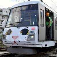 Railway workers attend to Tokyu Corp.’s new manekineko (beckoning cat) tram, which was unveiled Monday to commemorate the 110th anniversary of the Tamagawa Line, one of only two tram lines still operating in the capital. Tokyu unveils new tram with beckoning cat livery to mark 110th anniversary of Tamagawa Line
