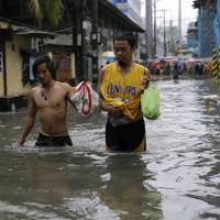 Residents wade though a flooded street in Manila on Tuesday after heavy rains swamped low-lying areas. Asian cities' endless summer