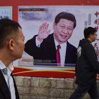 People walk past a poster featuring Chinese President Xi Jinping with a slogan reading “Chinese Dream, People’s Dream” in Beijing on Monday. Sino-Japanese rivalry deepens as Abe and Xi look set to consolidate grips on power