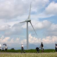 People walk past a turbine at the Electric Power Development Co. wind farm near the city of Koriyama, Fukushima Prefecture in August 2012. Balance of power: Shift toward renewable energy appears to be picking up steam