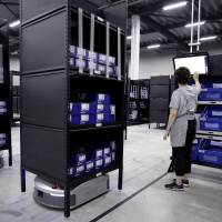 An employee types on a touch screen as a Geek Inc. Eve robot transports shelves at Acca International Co. warehouse in Inzai, Chiba Prefecture, on Sept. 7. Japan's robots stepping up to fill worst labor shortage in 40 years