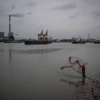 A man fishes with a net across from the Wujing Coal-Electricity Power Station in Shanghai in February. With plant closures, China is stepping up its massive antipollution campaign. Top polluter China unveils nationwide carbon market