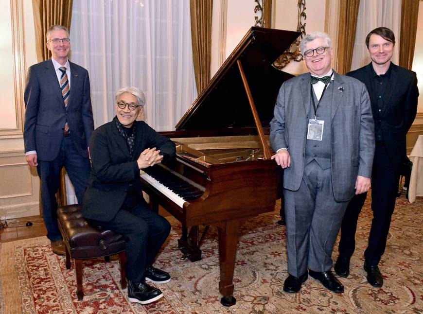 Ryuichi Sakamoto (seated at the piano) attends a reception on Dec. 14 at the Canadian Embassy with (from left) Canadian Ambassador Ian Burney; Brian Levine, executive director of The Glenn Gould Foundation; and electronic musician Scott Morgan. Sakamoto curated 