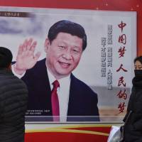 People walk past a poster of Chinese President Xi Jinping in Beijing on Monday. Xi’s tightening grip on China had already earned the leader comparisons to Mao Zedong, but they came into even sharper focus after the party on Sunday paved the way for him to assume the presidency indefinitely. Why 'Emperor Xi' should worry