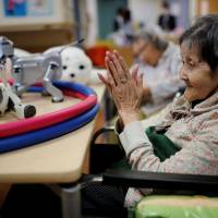 A resident claps to call Aibo, a robotic dog, at Shintomi nursing home in Tokyo. Robots making inroads in Japan's elder care facilities, but costs still high