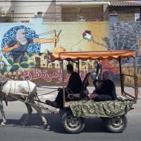 Palestinians ride in a donkey cart past graffiti showing U.S. President Donald Trump with a footprint on his face and Arabic that reads, “For al-Quds (Jerusalem) and the right of return we resist,” in Gaza City Sunday. Palestinian, 20, in 'very risky' critical condition after he publicly sets himself on fire in Gaza