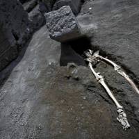 The legs of a skeleton emerge from the ground beneath a large rock believed to have crushed the victim’s bust during the eruption of Mount Vesuvius in A.D. 79, at Pompeii’s archeological site, near Naples, Italy, on Tuesday. New Pompeii discovery shows man crushed trying to flee eruption
