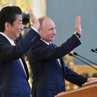 During their meeting in the Kremlin in Moscow on Saturday, Prime Minister Shinzo Abe and Russian President Vladimir Putin wave while talking to astronauts aboard the International Space Station. Abe continues balancing act with Putin as he chases peace treaty, disputed isles at Moscow summit