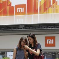 Women use a smartphone outside a Xiaomi store in Hong Kong on Wednesday. Chinese startup Xiaomi prepares for Hong Kong IPO as it sets out to challenge Google and Amazon
