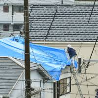 A man covers a damaged roof with a blue plastic sheet in Takatsuki, Osaka Prefecture, on Wednesday after a big earthquake rocked the area last Monday morning. Local authorities say more than 6,000 structures were damaged in recent Osaka earthquake