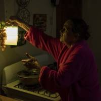 Marta Bermudez Robles, 66, hangs a lamp in her kitchen in Adjuntas, Puerto Rico, on July 12, 2018, at her home that is still with electricity since hurricanes Irma and Maria. The only power Bermudez and her husband have had for 10 months is courtesy of a neighbor who threw over an extension cord connected to his generator. It provides just enough power to light one bulb in the kitchen and another in the living room for a couple hours each day. Almost a year after hurricanes Irma and Maria, Puerto Ricans are finally seeing power restored