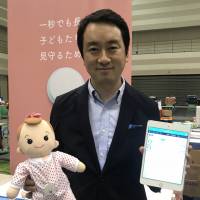 Unifa Inc. President Yasuyuki Toki shows off a tablet and a sensor, modelled using a doll, that can be used to monitor sleeping infants at nursery schools. Nagoya firm's high-tech service aims to prevent sudden infant death syndrome at nursery schools