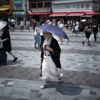 An elderly woman holds an umbrella to shield herself from sunlight as she walks along a street in Tokyo. As Japan endures record heat wave, large population of elderly at highest risk