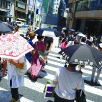 People carrying parasols walk across a pedestrian crossing in Tokyo on Friday. Q&A: How to survive this year's scorching summer in Japan
