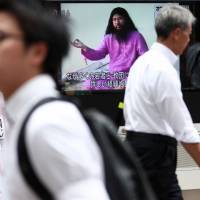 Pedestrians in Tokyo on Thursday walk past a large screen showing Shoko Asahara, leader of the Aum Shinrikyo cult, following the execution of the last six members of the doomsday cult involved in the 1995 Tokyo subway sarin gas attack. Haruki Murakami says he cannot oppose execution of Aum cultists in '95 sarin attack
