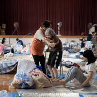 An elderly woman is given assistance as people affected by the recent flooding rest at a makeshift shelter at a gymnasium in the Mabicho district of Kurashiki, Okayama Prefecture, on Wednesday. Water outages continue in flood-hit areas across western Japan, as death toll tops 170