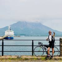 Final destination: The author poses triumphantly in front of the erupting Mount Sakurajima in Kagoshima Prefecture. Kyushu by bicycle: Love hotels, hot springs and rugged climbs