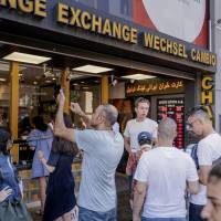 A tourist takes a photograph of the latest foreign currency rates posted outside an exchange bureau in Istanbul on Monday. Turkish lira crash may affect some Japanese companies with operations there