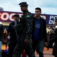 Army soldiers patrol a street next to people from Venezuela after checking their passports or identity cards at a border control in Roraima state, Brazil, on Aug. 19. Brazil sends army to border as Venezuelans flee crisis at home