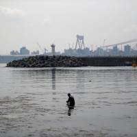A man wades through the water in front of a Hyundai Heavy Industries shipyard in Ulsan, South Korea, on May 29. South Korea's 'Hyundai Town' faces grim future with idled shipyard, rise in suicides