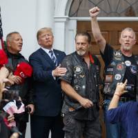 U.S. President Donald Trump stands in the rain with members of Bikers for Trump and supporters after saying the Pledge of Allegiance on Saturday at the clubhouse of Trump National Golf Club in Bedminster, New Jersey. One year after Charlottesville rally, Trump still flirts with racially tinged rhetoric