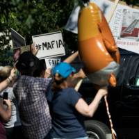 U.S. President Donald Trump rides past protesters as he leaves the Trump National Golf Club in Sterling, Virginia, to return to the White House on Saturday. As midterm elections loom, Republicans shrug off Trump's mounting woes for fear of alienating his base