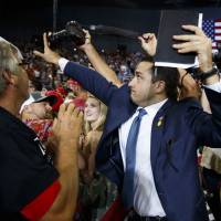 A volunteer member of the advance team for U.S. President Donald Trump blocks a camera as a photojournalist attempts to take a photo of a protester during a campaign rally at the Ford Center in Evansville, Indiana, on Thursday. In viral photo, Trump volunteer blocks news photographer's shot of protester
