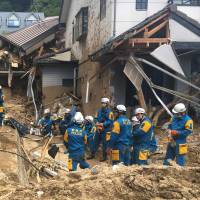 Emergency teams rest beside buildings damaged by flooding in Hiroshima Prefecture on July 9. Cabinet taps ¥105 billion in reserves to help rain-ravaged areas in west Japan