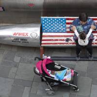 A woman tends to a child near a promotional gimmick in the form of a bomb and the U.S. flag outside a U.S. apparel shop in Beijing in April. China's trade surplus with U.S. hits record $31 billion in August