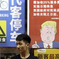 A man sits in front of a billboard stating that American customers will be charged 25 percent extra due to ongoing China-U.S. trade tensions at a restaurant in Guangzhou in southern China’s Guangdong Province on Aug. 13. China Party journal warns of trade war's impact on financial stability