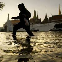 A woman walks through floodwaters in front of Bangkok’s Grand Palace near the Chao Praya River on Oct. 28, 2011, when the worst floods in decades left a fifth of the city underwater. With rising sea levels, Bangkok struggles to stay afloat
