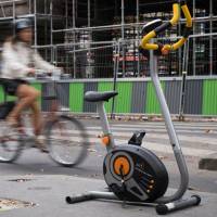 A cyclist passes by an exercise bike machine left on a sidewalk in Paris on Tuesday. Forty percent of Japanese adults face higher risk of disease from lack of exercise: WHO