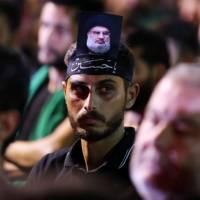 A supporter of Lebanon’s Hezbollah leader Sayyed Hassan Nasrallah has his picture on his head, during a live broadcast, the night before Muslim Shiites around the world mark the day of Ashura, in Beirut Wednesday. Hezbollah chief says group will stay in Syria till further notice but will pare ranks as 'great calm' sets in