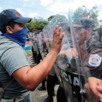 A masked anti-government protester shouts slogans to riot police during a protest over Nicaraguan President Daniel Ortega’s government in Managua Sunday. Thousands stage anti-Ortega protest in Managua, demand release of hundreds