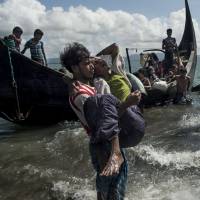 A Bangladeshi man helps Rohingya Muslim refugees tdisembark from a boat on the Bangladeshi shoreline of the Naf river after crossing the border from Myanmar in Teknaf last September. The International Criminal Court said Thursday it had jurisdiction to probe the forced deportation of Rohingya Muslims by Myanmar’s military as a possible crime against humanity. Judges rule ICC has jurisdiction over Myanmar's expulsions of Rohingya masses