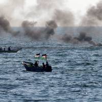 Palestinians sail with boats towards the maritime border with Israel as smoke rises from a burning tire during a protest calling for lifting the Israeli blockade on Gaza, in the Mediterranean Sea off the coast of the northern Gaza Strip Monday. U.S. ups pressure on Palestinians, closing Washington PLO mission
