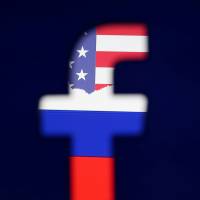 American and Russian flags are seen through a 3D-printed logo for Facebook, one of the companies that face possible U.S. antitrust investigations. White House order would crack down on Google and Facebook's business practices